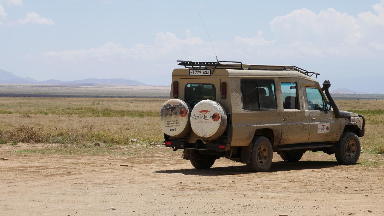 A single safari vehicle small against a wide, empty plain