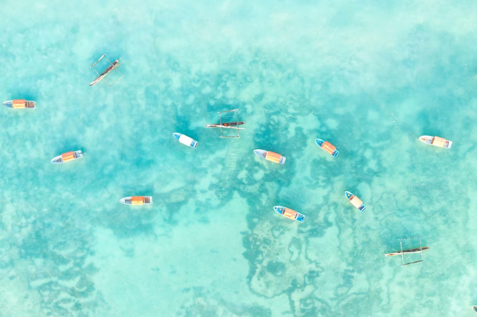 Dhows and outrigger boats at anchor over pale turquoise shallows off Zanzibar, seen from above